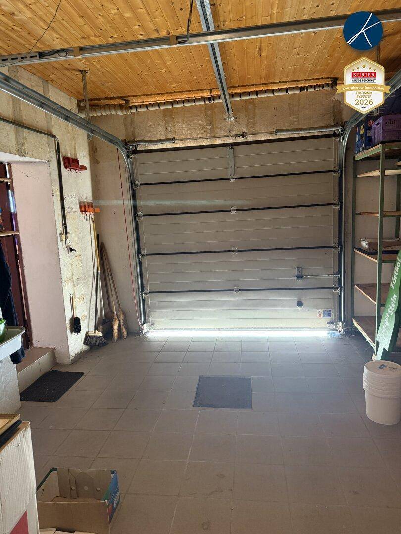 Geräumige Garage mit Rolltor, Fliesenboden und Holzdecke, bietet praktischen Stauraum.