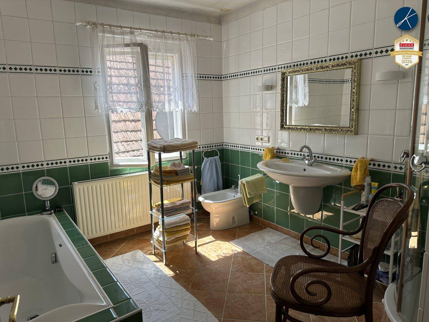 Badezimmer mit grünen und weißen Fliesen, Badewanne, Bidet und einem Fenster für Tageslicht.