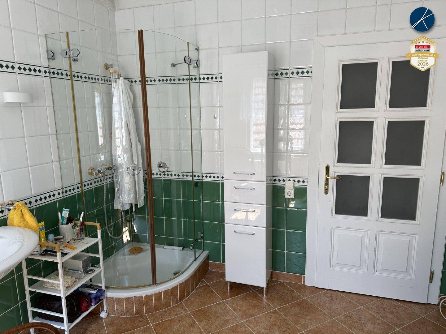 Badezimmer mit Duschkabine, grünen Fliesen und einem weißen Hochschrank für Stauraum.