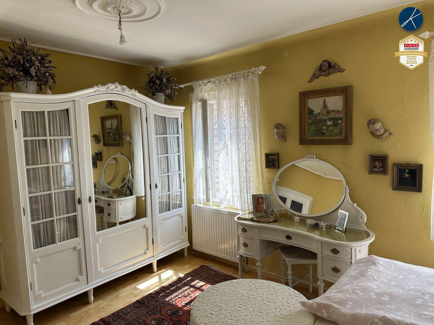Schlafzimmer mit gelben Wänden, weißem Kleiderschrank und elegantem Schminktisch mit Spiegel.