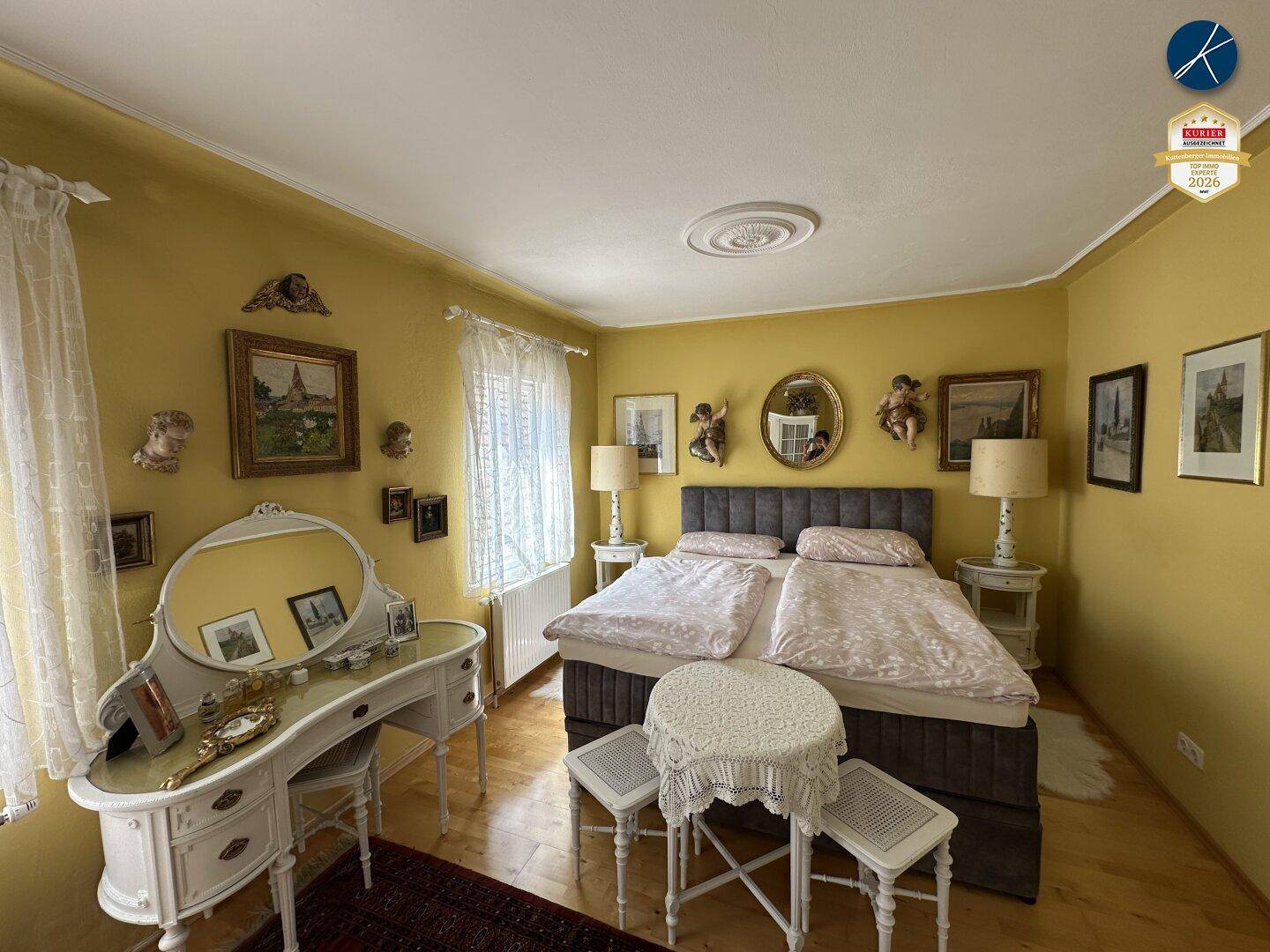 Helles Schlafzimmer mit gelben Wänden, Doppelbett und klassischem weißen Schminktisch am Fenster.