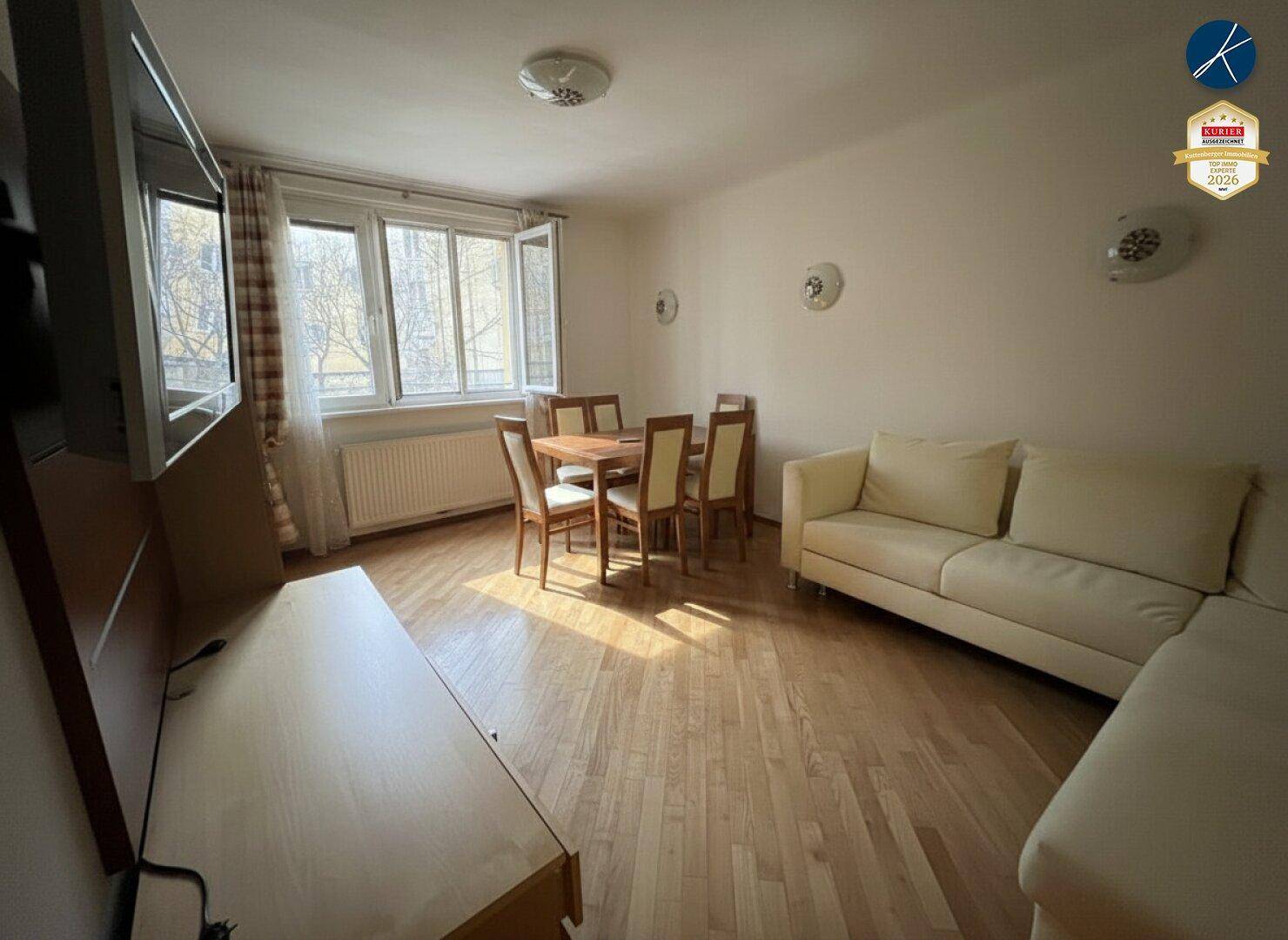 Gemütlicher Wohn-Essbereich mit Holzboden, Esstisch und Sofa, gut beleuchtet durch ein Fenster.