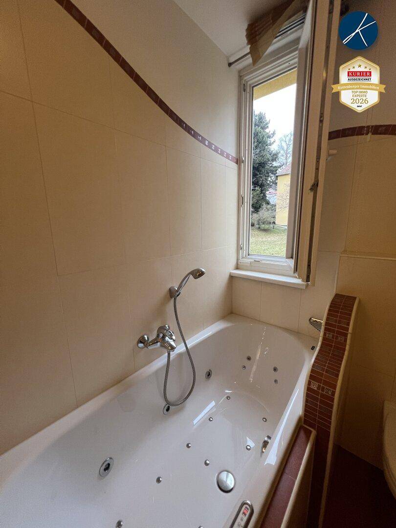 Badewanne mit Whirlpool-Funktion und Fensterblick ins Grüne in einem gefliesten Badezimmer.