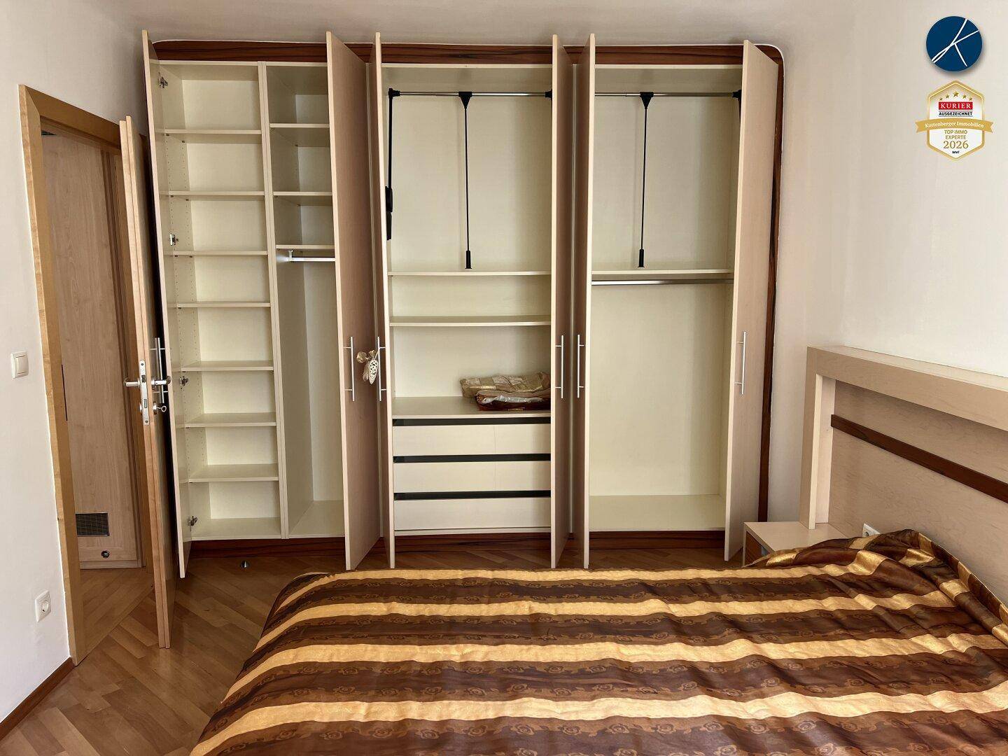 Schlafzimmer mit geöffnetem Einbauschrank, der Regale und Kleiderstangen zeigt.