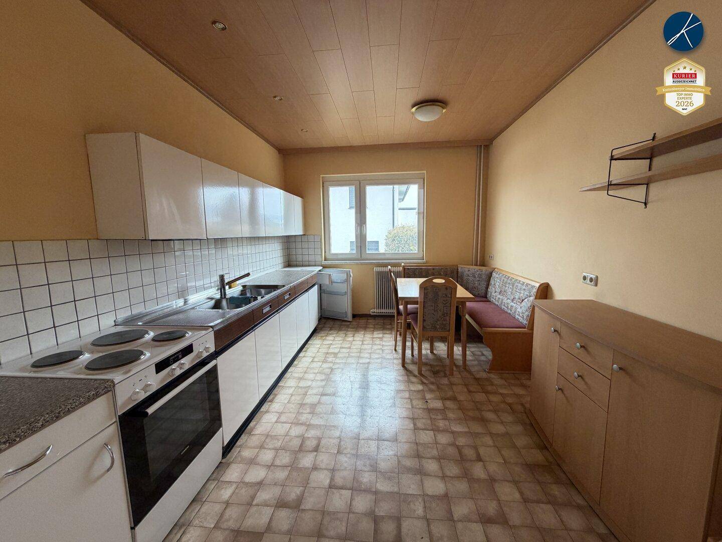 Funktionale Küche mit weißen Schränken, Fliesenboden und einer gemütlichen Essecke am Fenster.