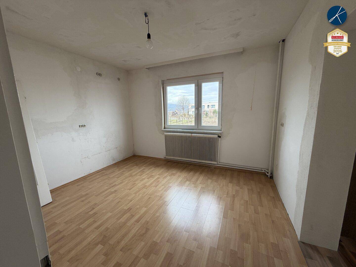 Helles Schlafzimmer mit hellem Holzboden, weißen Wänden und einem Fenster, das viel Tageslicht hereinlässt.