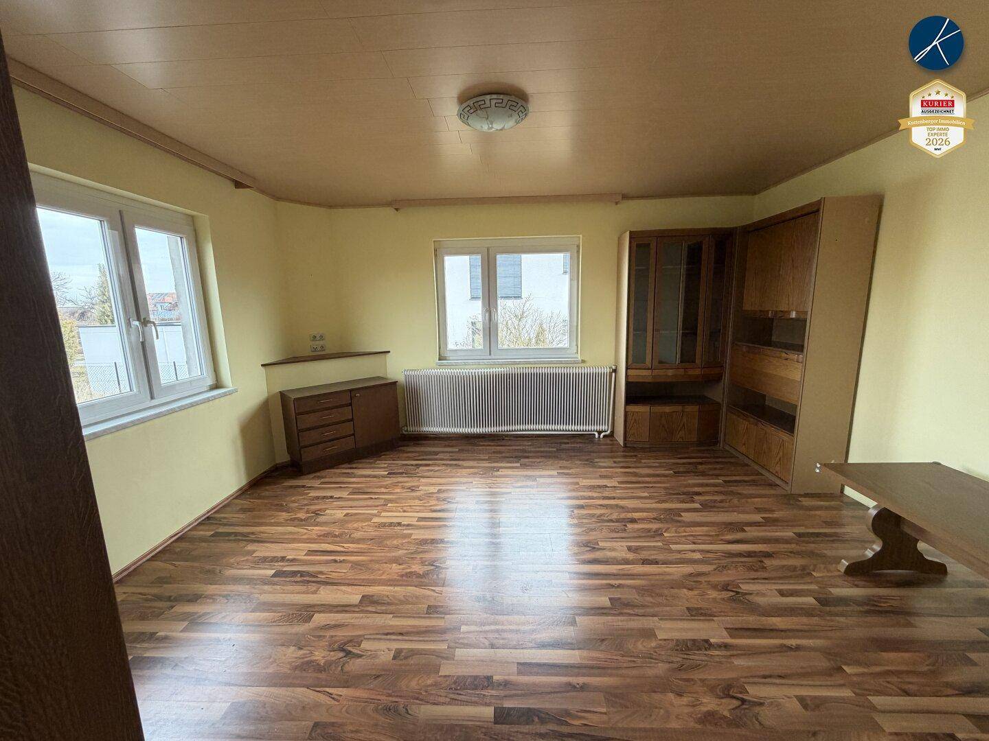 Geräumiges Wohnzimmer mit Laminatboden, gelben Wänden und großen Fenstern, bereit zur individuellen Gestaltung.