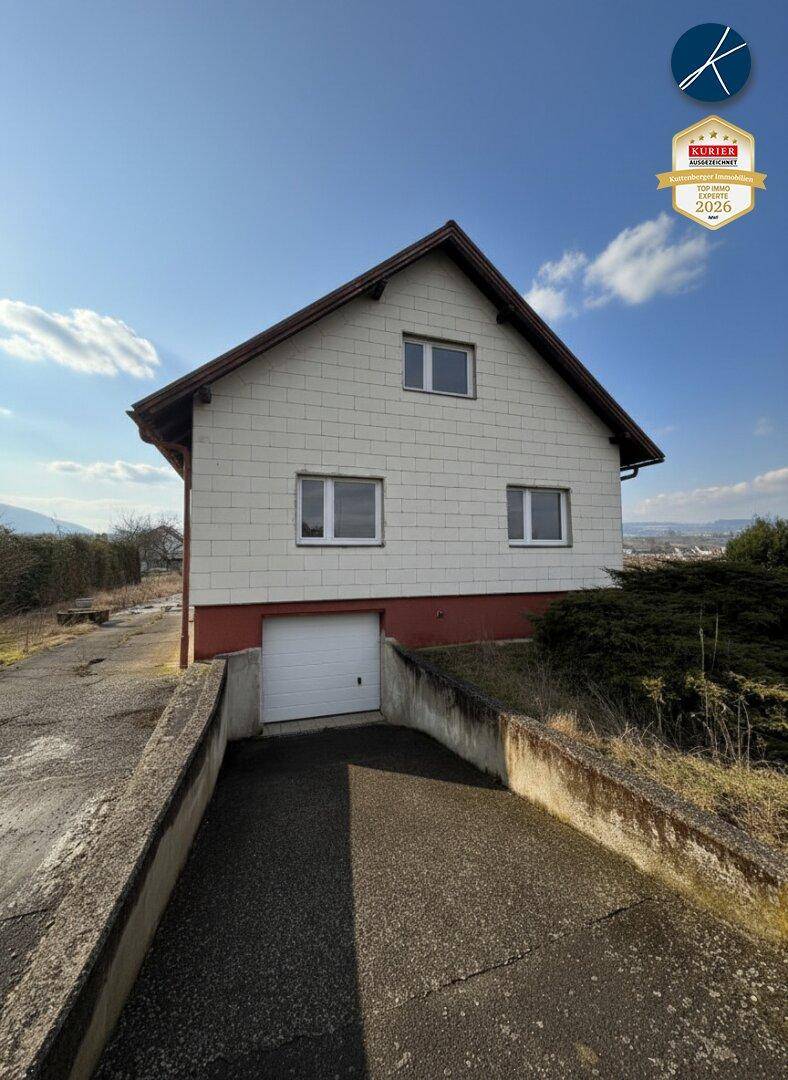 Einfamilienhaus mit weißer Fassade, rotem Sockel und integrierter Garage, umgeben von einer Auffahrt.