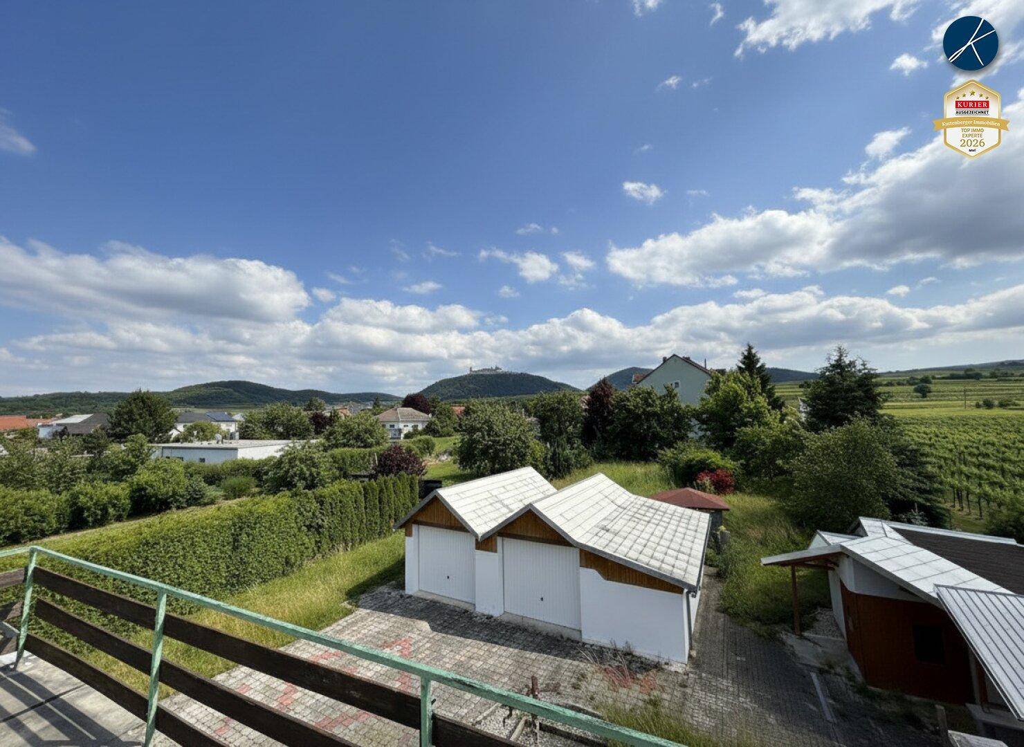 Blick von oben auf zwei Garagen und die umliegende ländliche Bebauung mit Weinbergen im Hintergrund.
