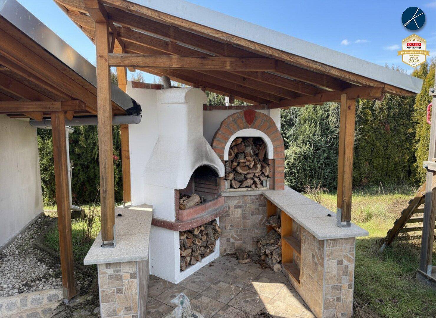 Überdachter Außenbereich mit gemauertem Grill, Pizzaofen und Arbeitsflächen, ideal für gesellige Abende.
