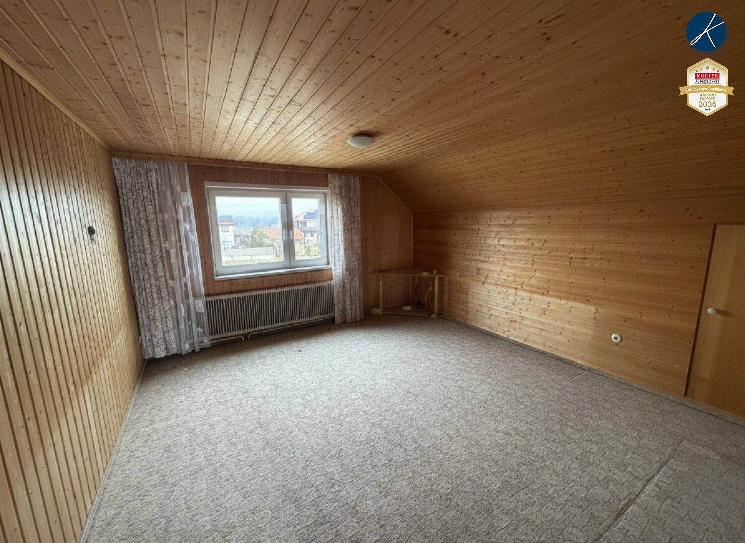 Gemütliches Zimmer mit Holzvertäfelung an Wänden und Decke, Teppichboden und einem Fenster.