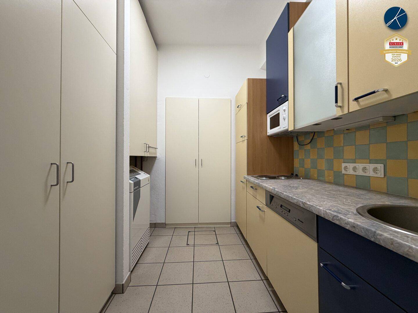 Schmale Küche mit hellen Schränken, Fliesenboden, Spülmaschine und Waschmaschine.