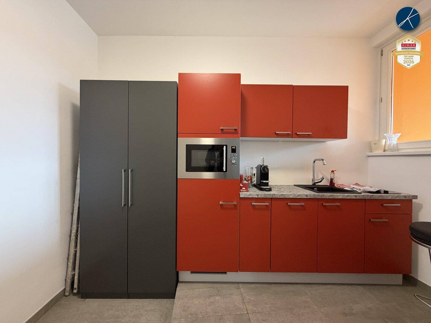 Moderne Küchenzeile mit roten und grauen Schränken, Mikrowelle und Spülbecken.