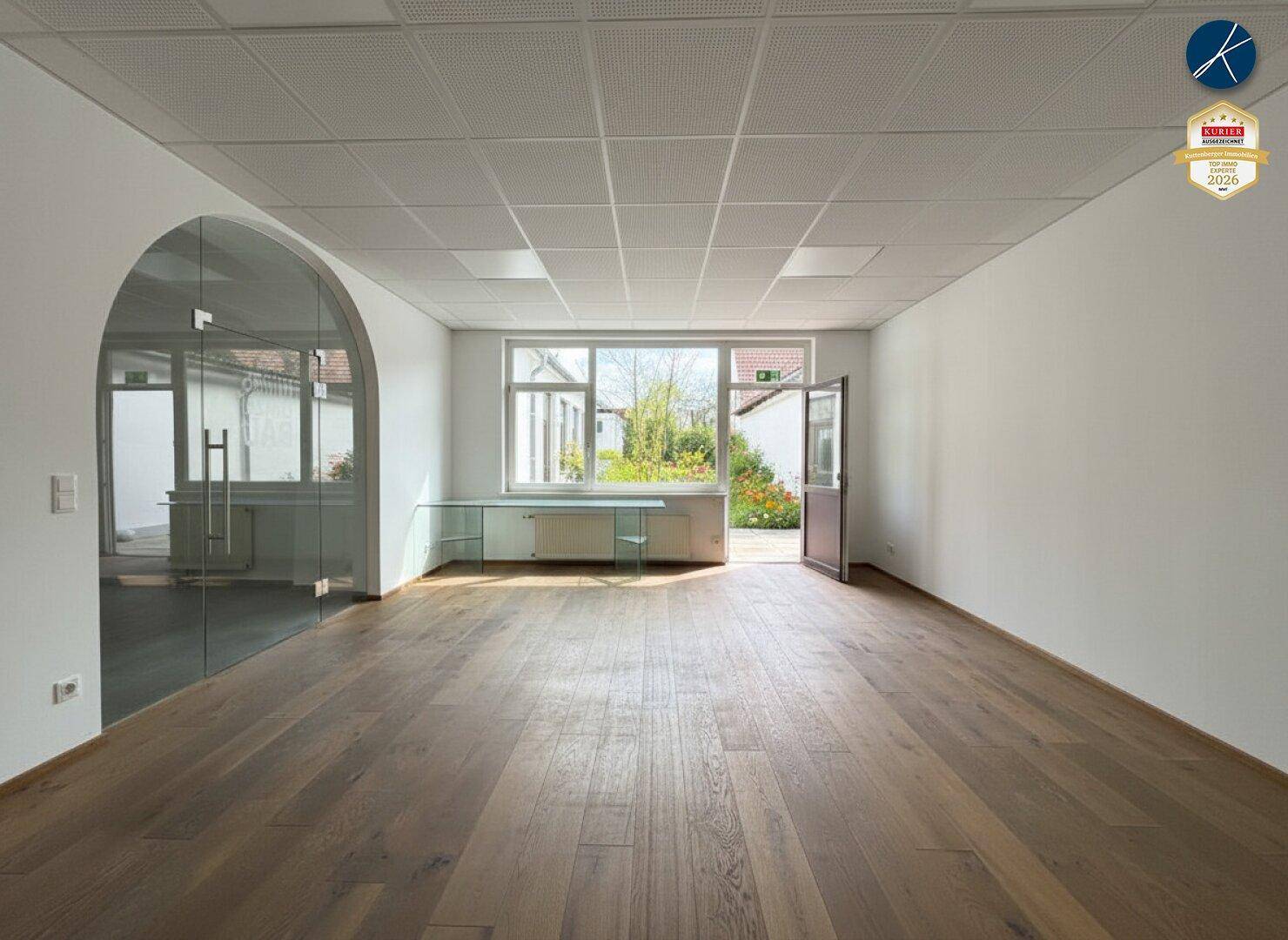 Helles Büro mit Holzboden, großen Fenstern und Zugang zu einem kleinen Innenhof.