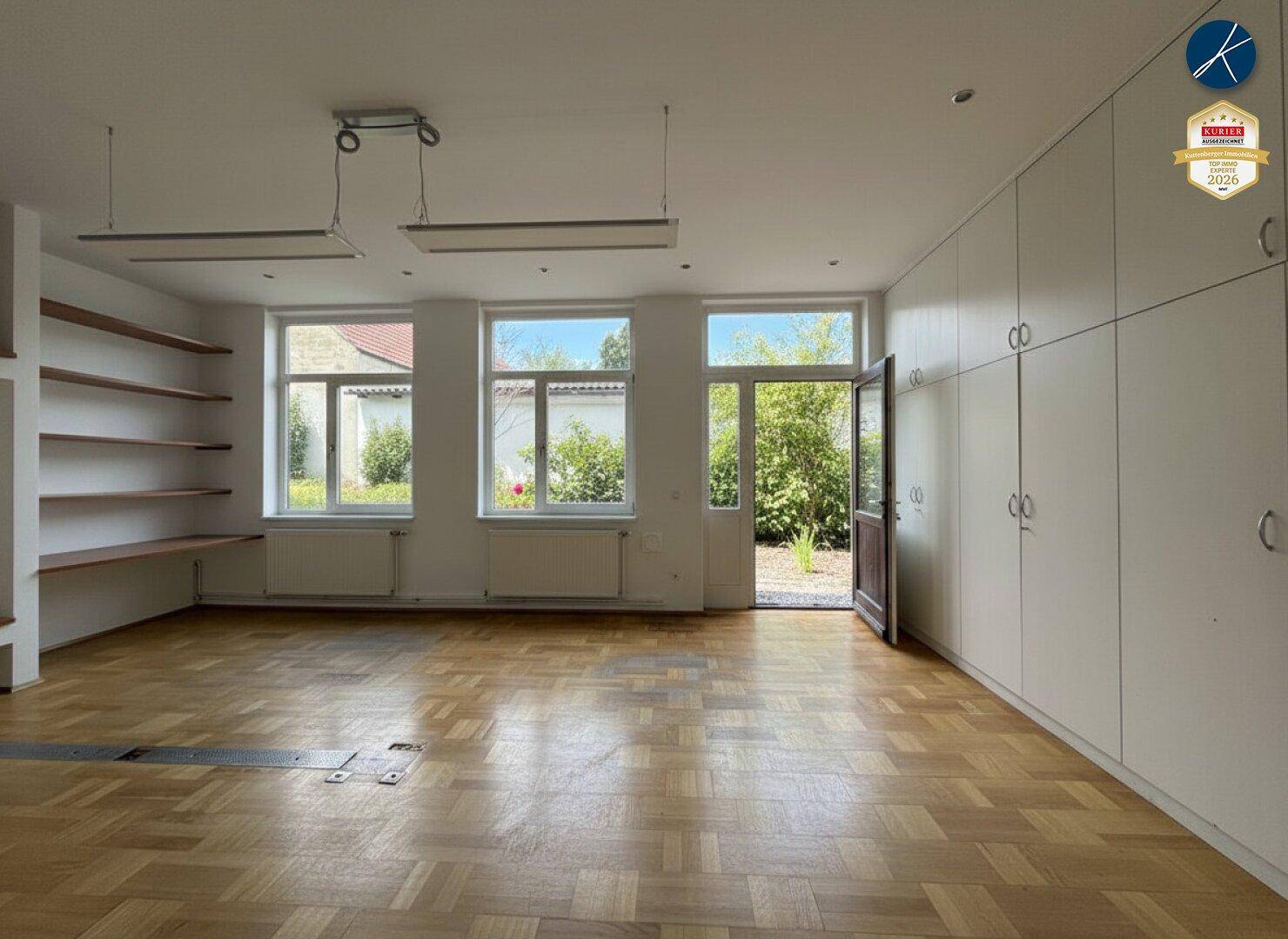 Geräumiger Raum mit Einbauschränken, Holzparkett und Zugang zu einem kleinen Gartenbereich.