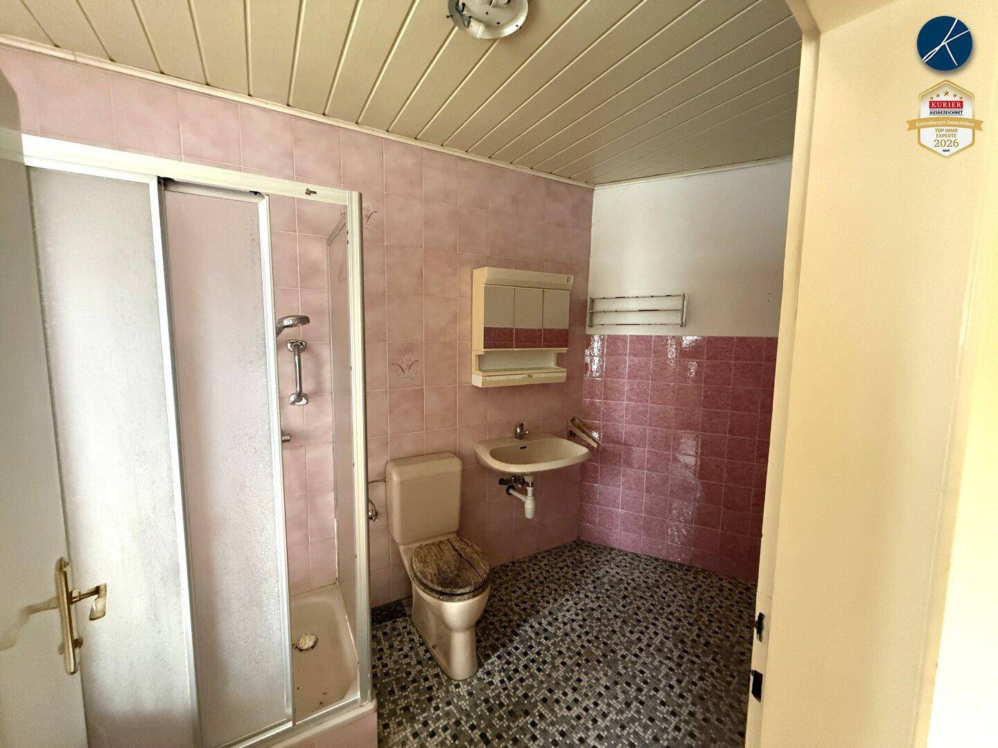 Badezimmer mit rosa Fliesen, Duschkabine, Toilette und Waschbecken, im Stil der 80er Jahre.