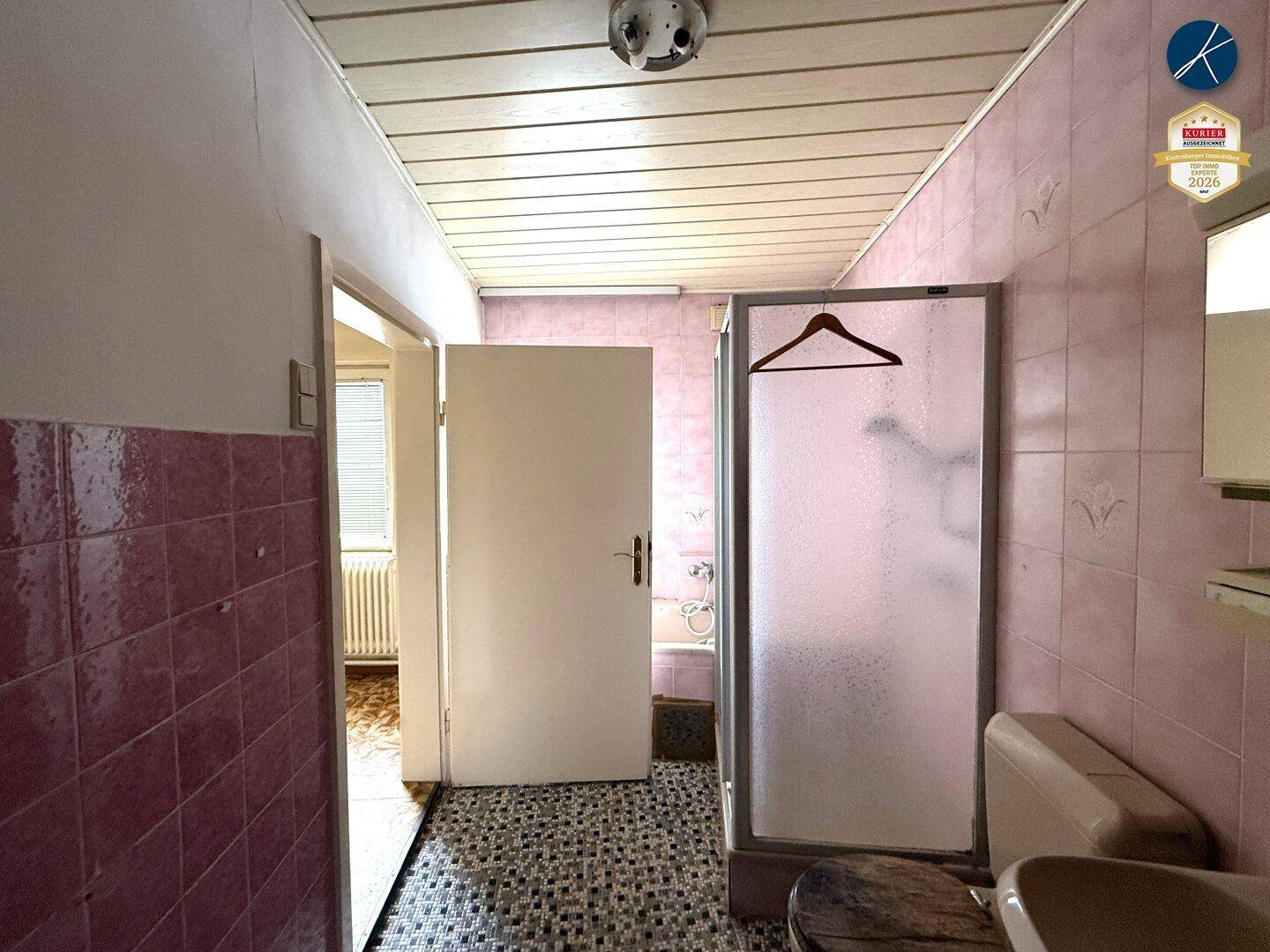 Weiterer Blick ins Badezimmer mit Duschkabine und rosa Fliesen, die den Raum prägen.