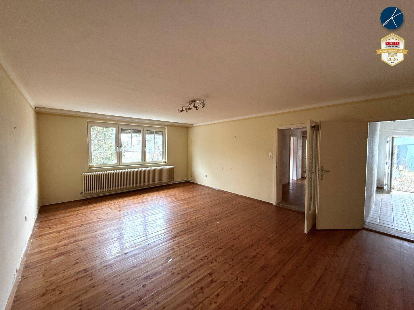 Geräumiges Wohnzimmer mit Holzdielenboden, gelben Wänden und großem Fenster für viel Tageslicht.