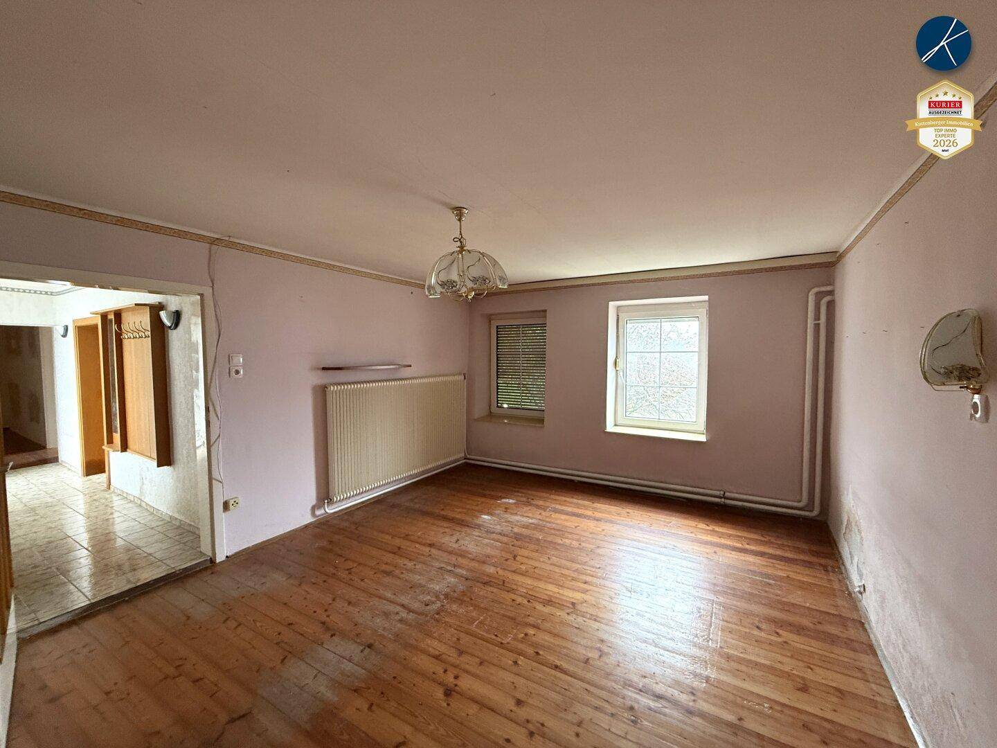 Schlafzimmer mit Holzdielenboden, rosa Wänden und einem Fenster, das Tageslicht hereinlässt.
