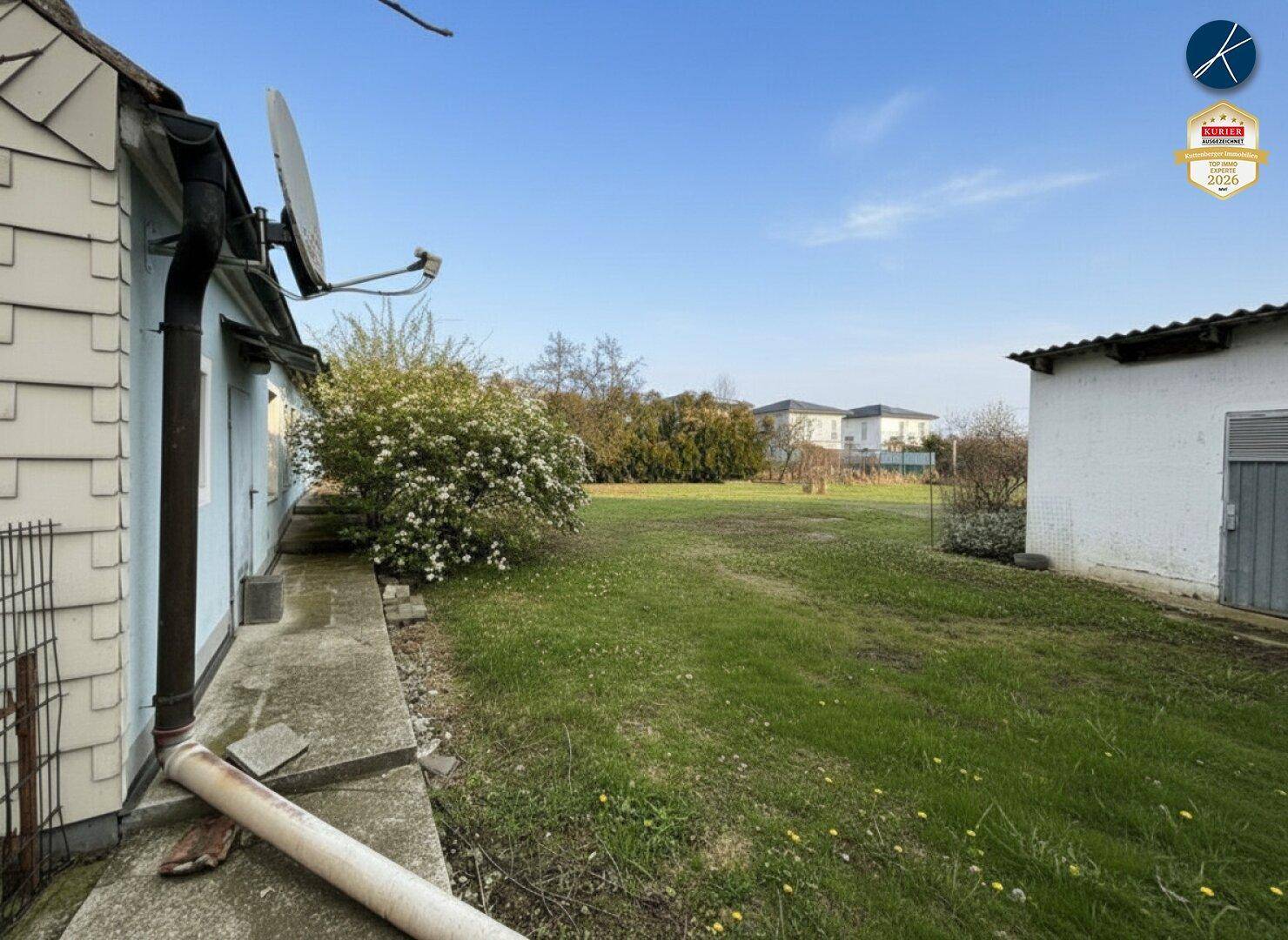 Seitenansicht des Hauses mit grünem Rasen und einem kleinen Nebengebäude unter klarem Himmel.