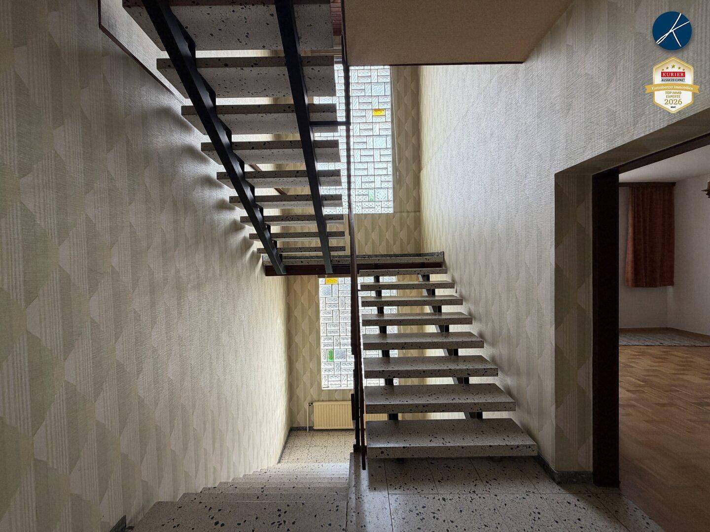 Treppenhaus mit Terrazzoboden, gemusterter Tapete und Glasbausteinen für natürliches Licht.