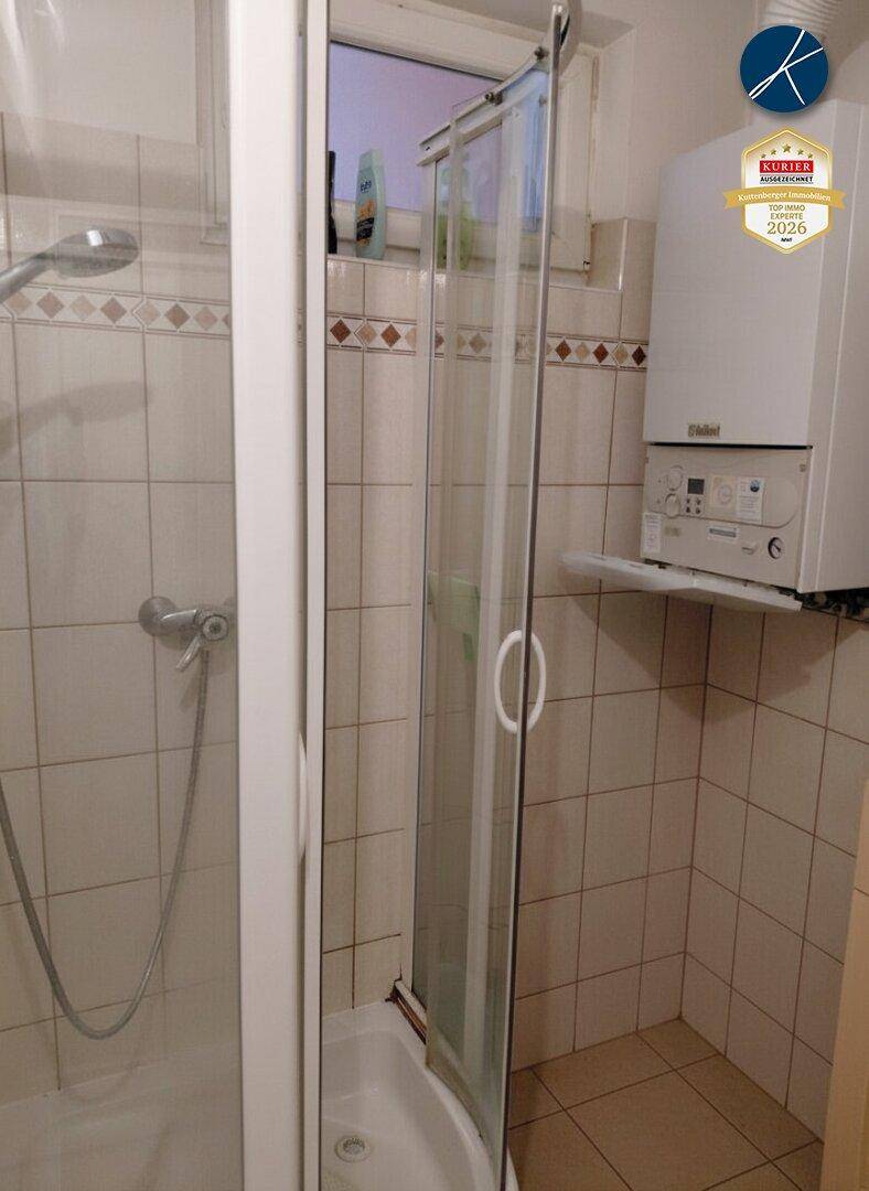 Kleines Badezimmer mit Duschkabine, Fliesen und einem wandmontierten Warmwasserbereiter.