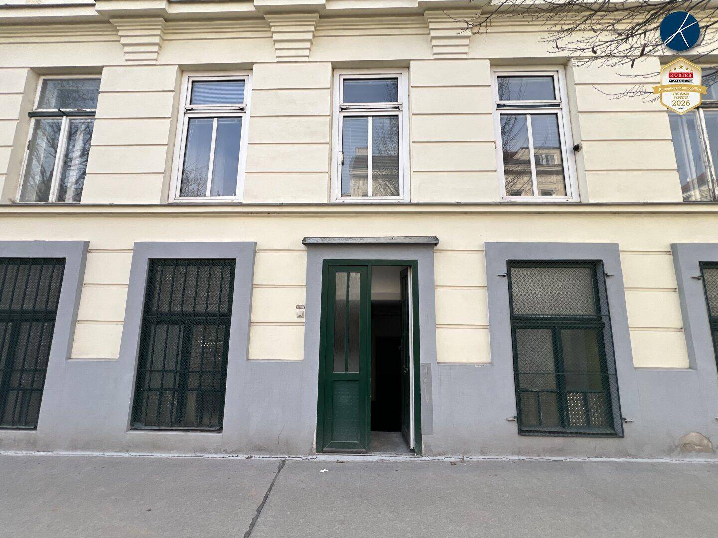 Eingangsbereich des Gebäudes mit grüner Tür und vergitterten Fenstern im Erdgeschoss.