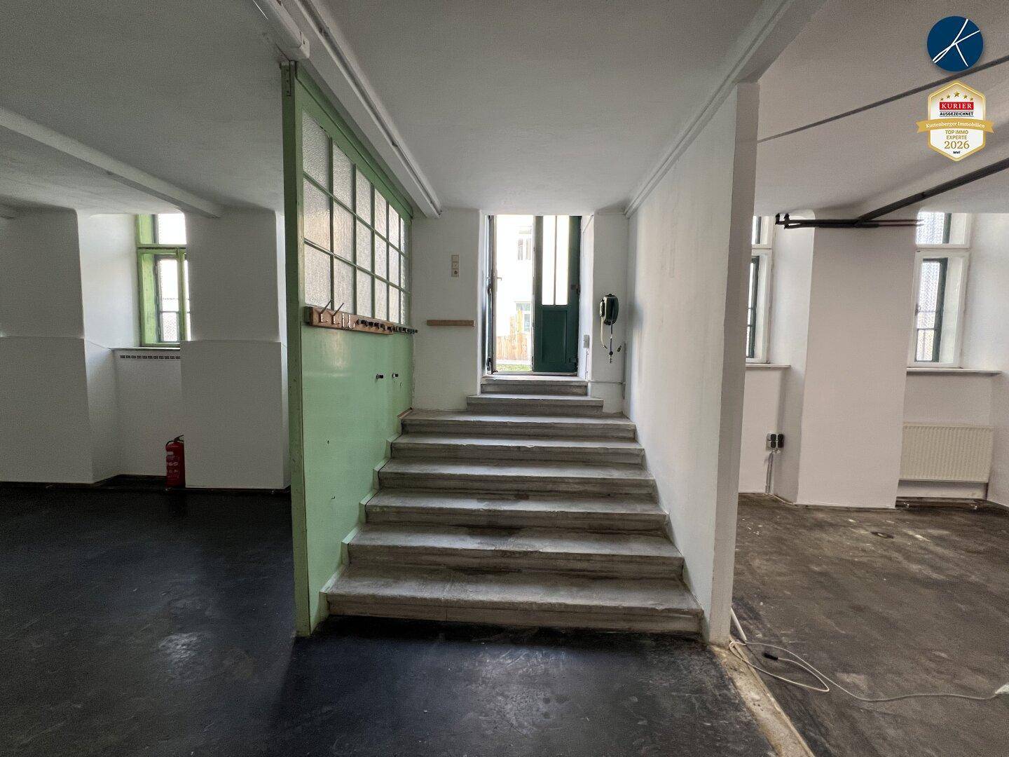 Eingangsbereich mit Treppe, grüner Glasabtrennung und Zugang zum Hauptgebäude.