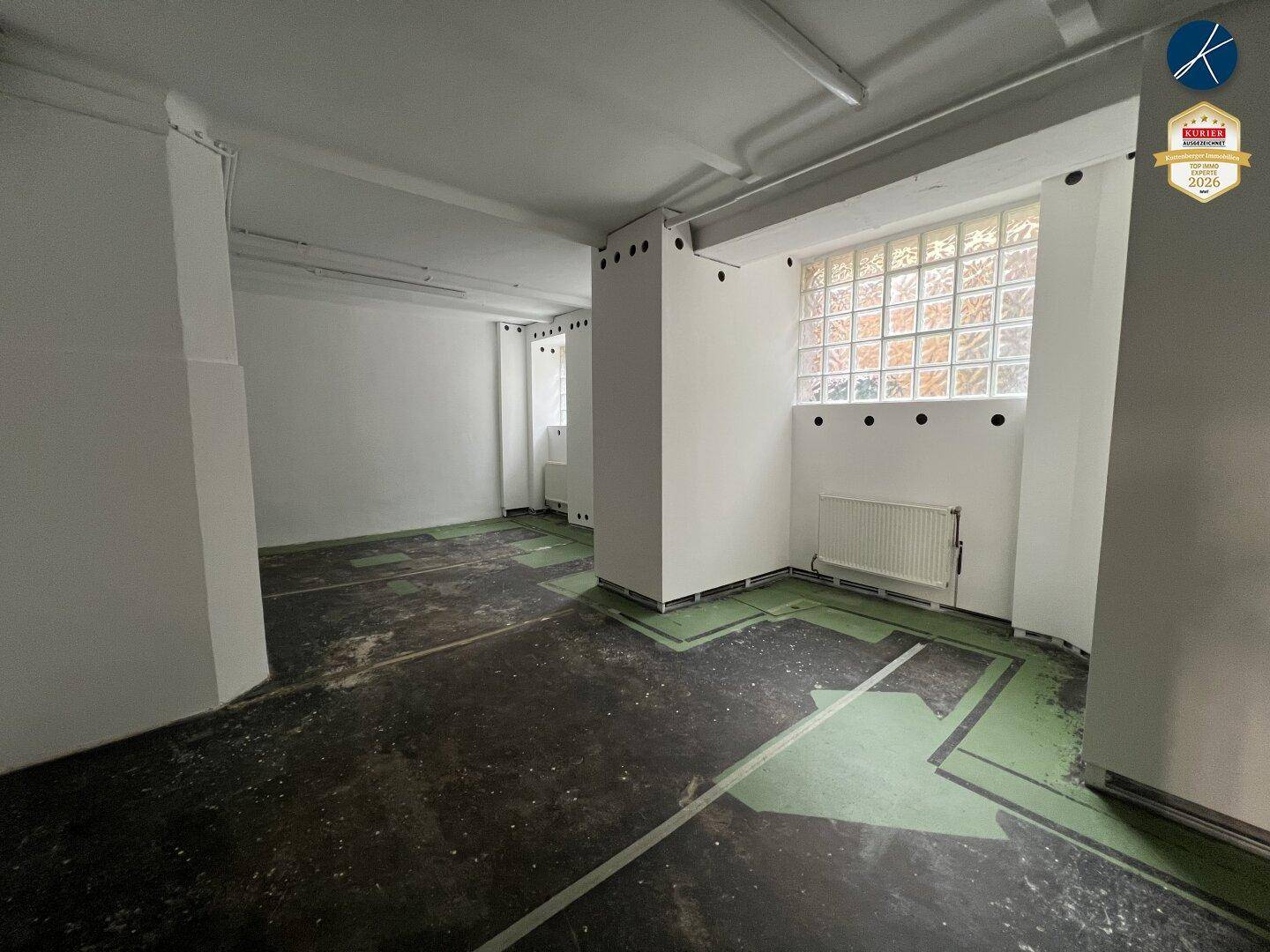 Geräumiger Gewerberaum mit Glasbausteinfenstern, weißen Wänden und grünen Bodenmarkierungen.