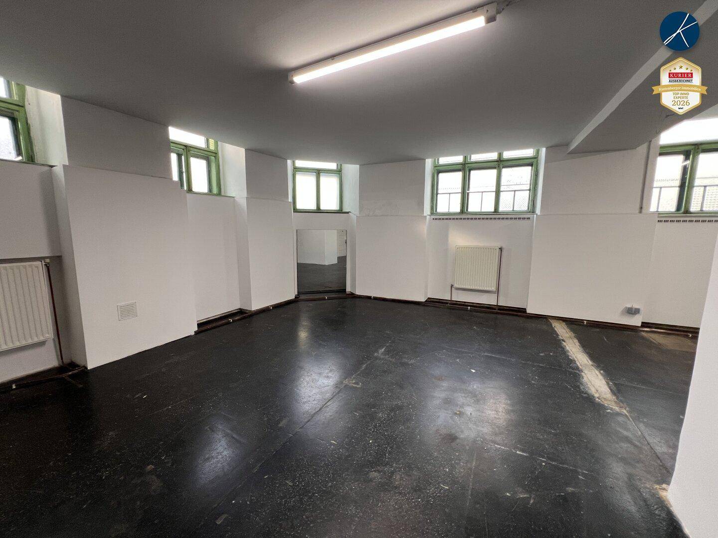 Heller Gewerberaum mit vielen Fenstern, Spiegeln und dunklem Industrieboden.