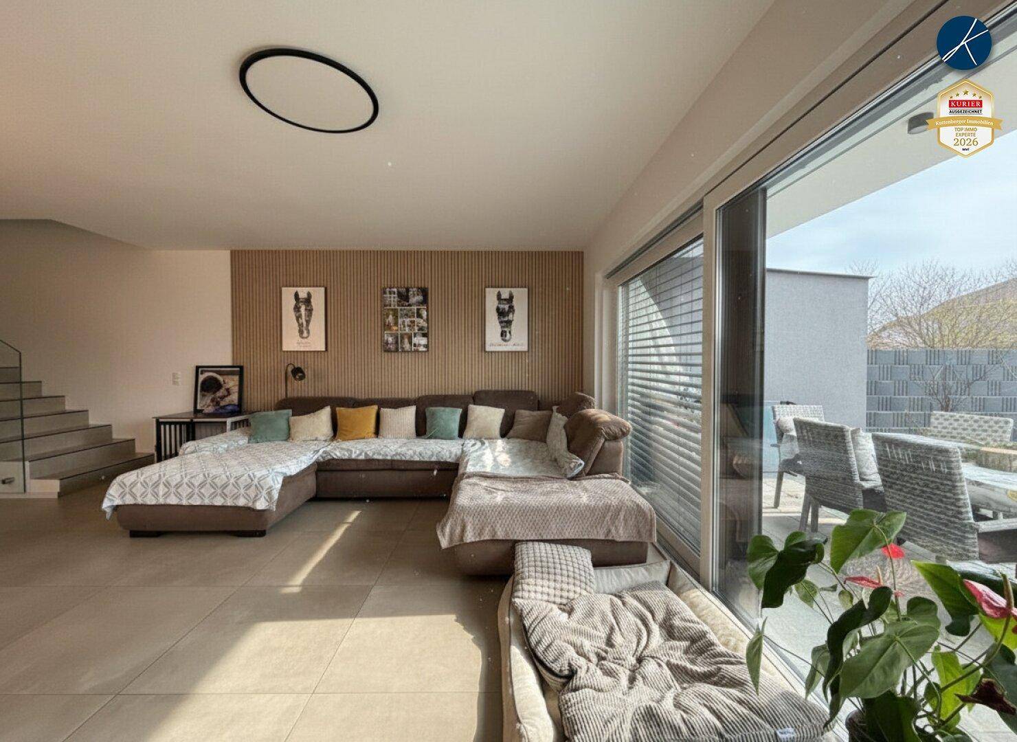 Helles Wohnzimmer mit großem Sofa, Holzwand und Zugang zur Terrasse.