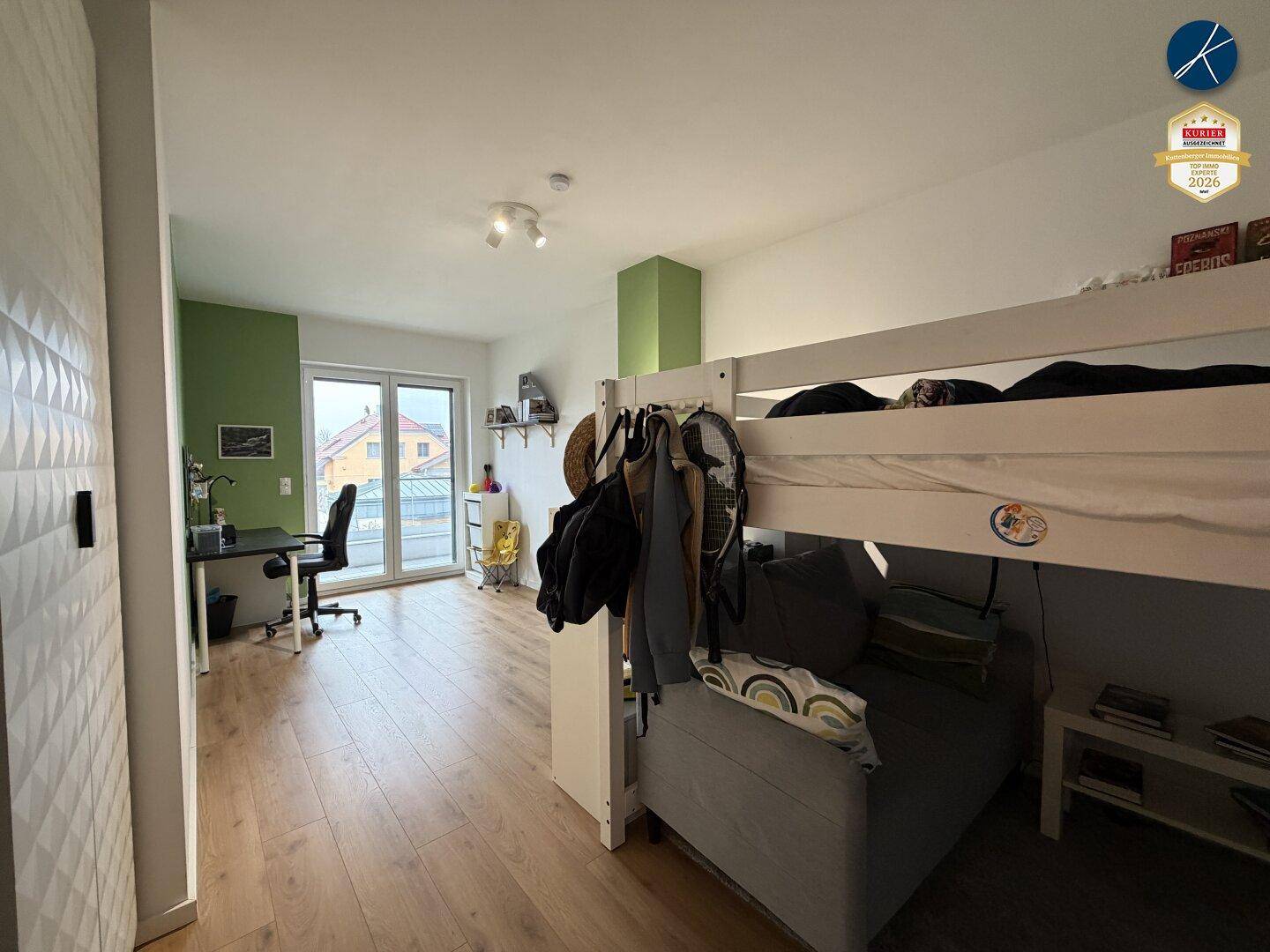 Kinderzimmer mit Etagenbett, Schreibtisch und Zugang zu einem kleinen Balkon.