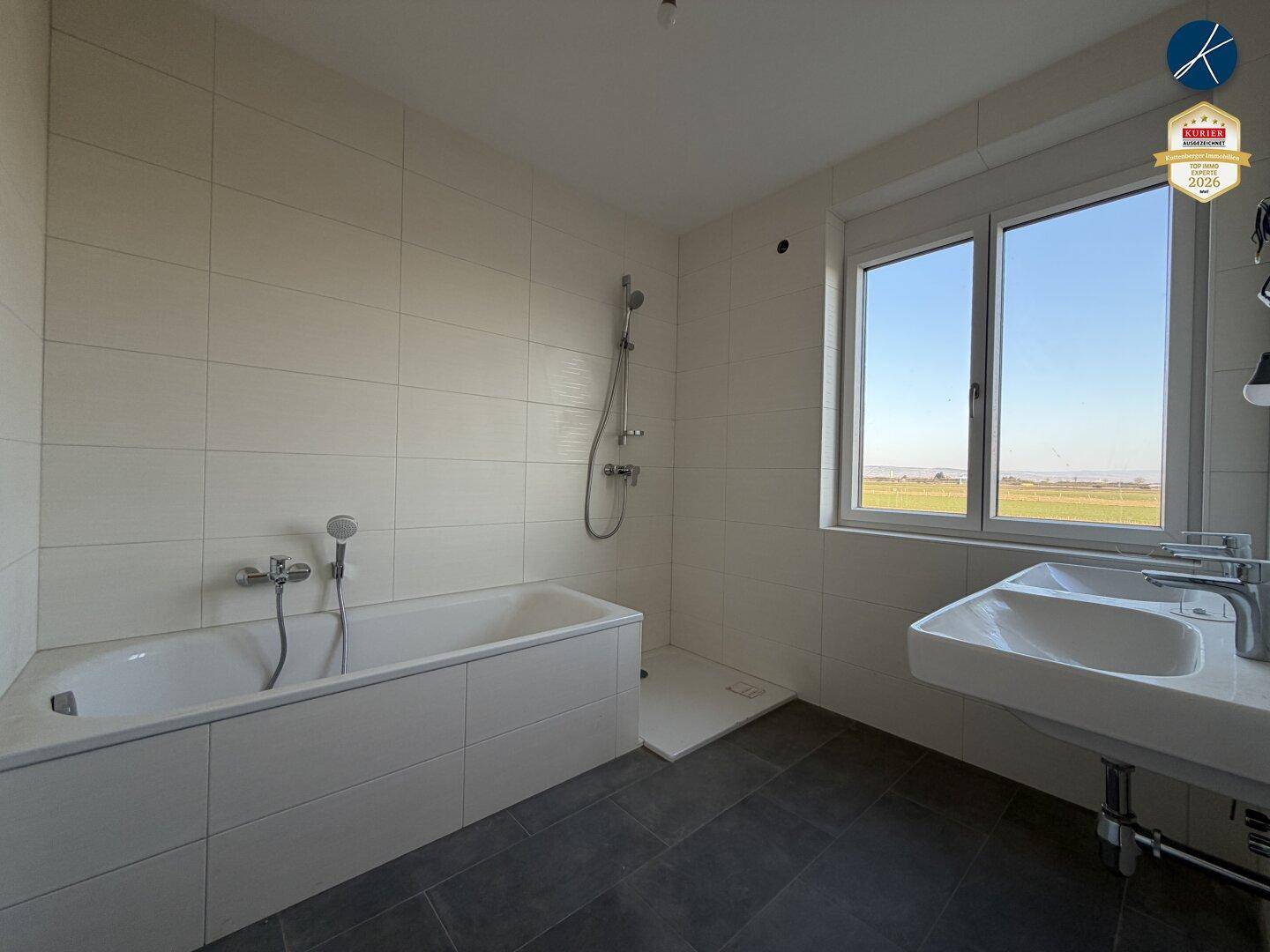 Modernes Badezimmer mit Badewanne, Dusche, Doppelwaschbecken und weitem Blick ins Grüne.