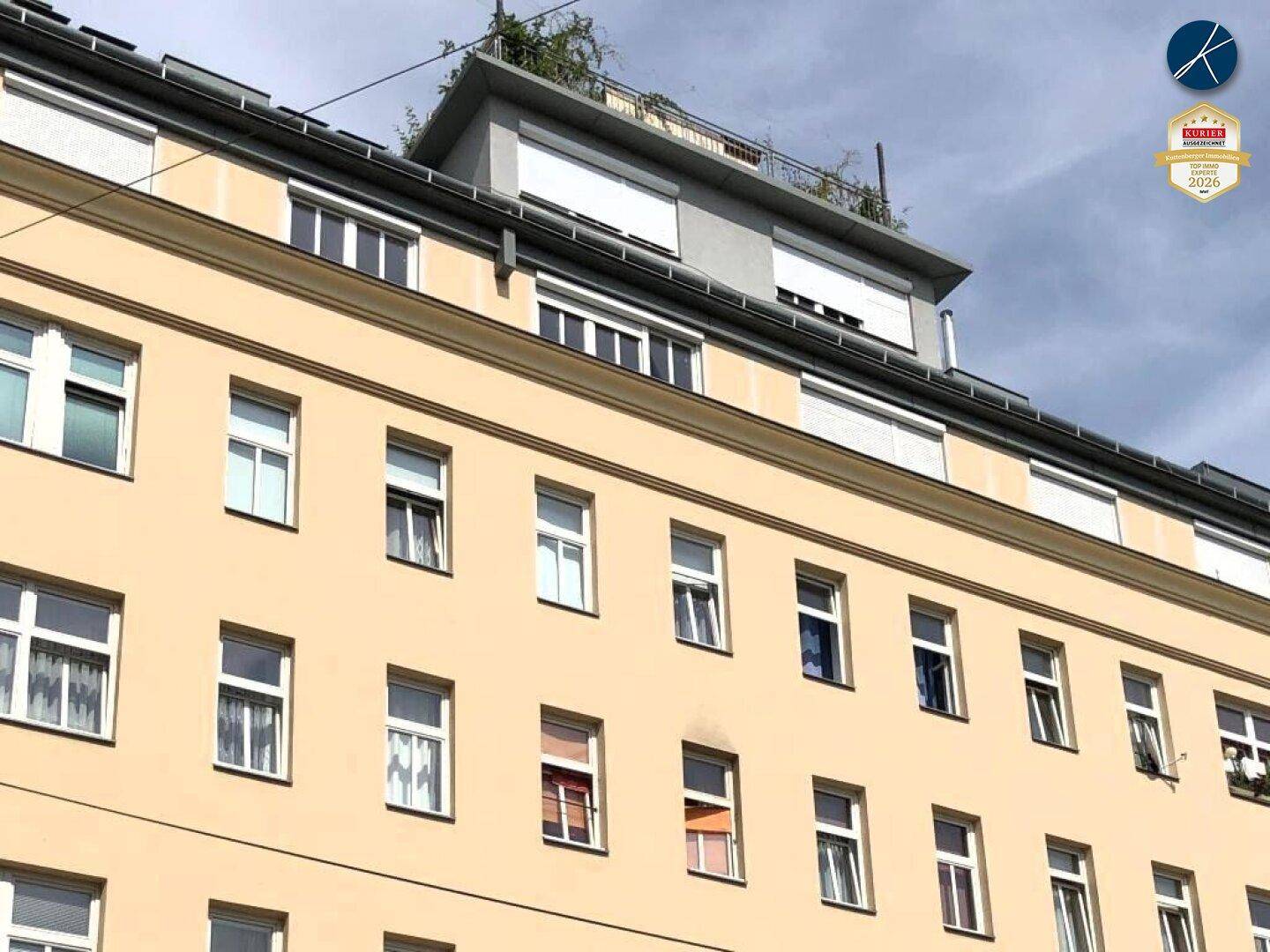Seitenansicht der Gebäudefassade mit zahlreichen Fenstern und einem begrünten Dachaufbau unter blauem Himmel.