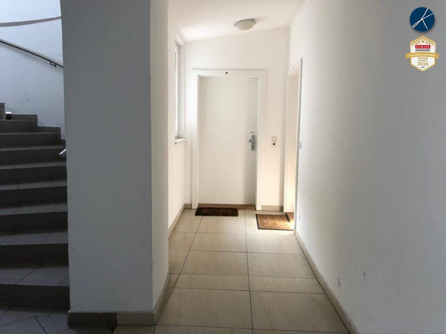 Heller Flur mit Treppenaufgang und weißer Wohnungstür, die zu den oberen Etagen führt.