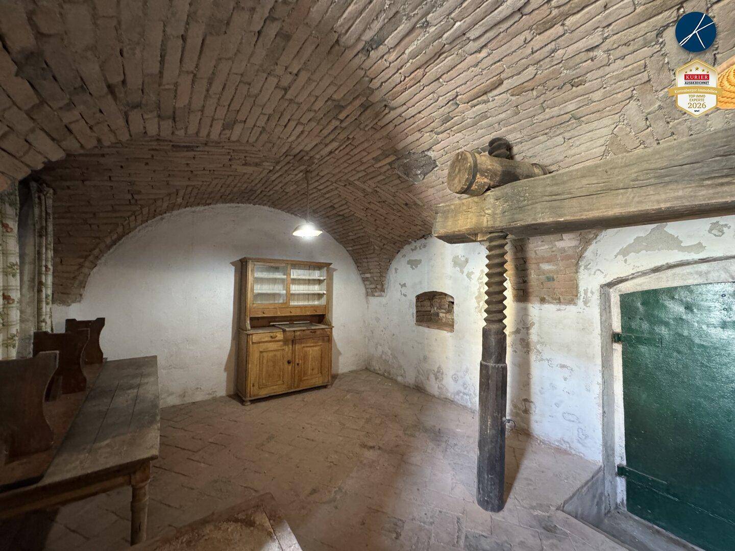 Historischer Kellerraum mit Ziegelgewölbe, altem Holzschrank und einer traditionellen Weinpresse.