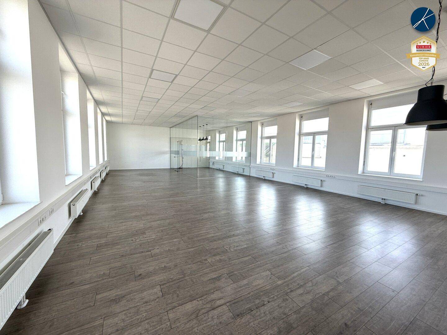 Geräumiges, leeres Büro mit vielen Fenstern und modernem Laminatboden, bereit zur individuellen Gestaltung.
