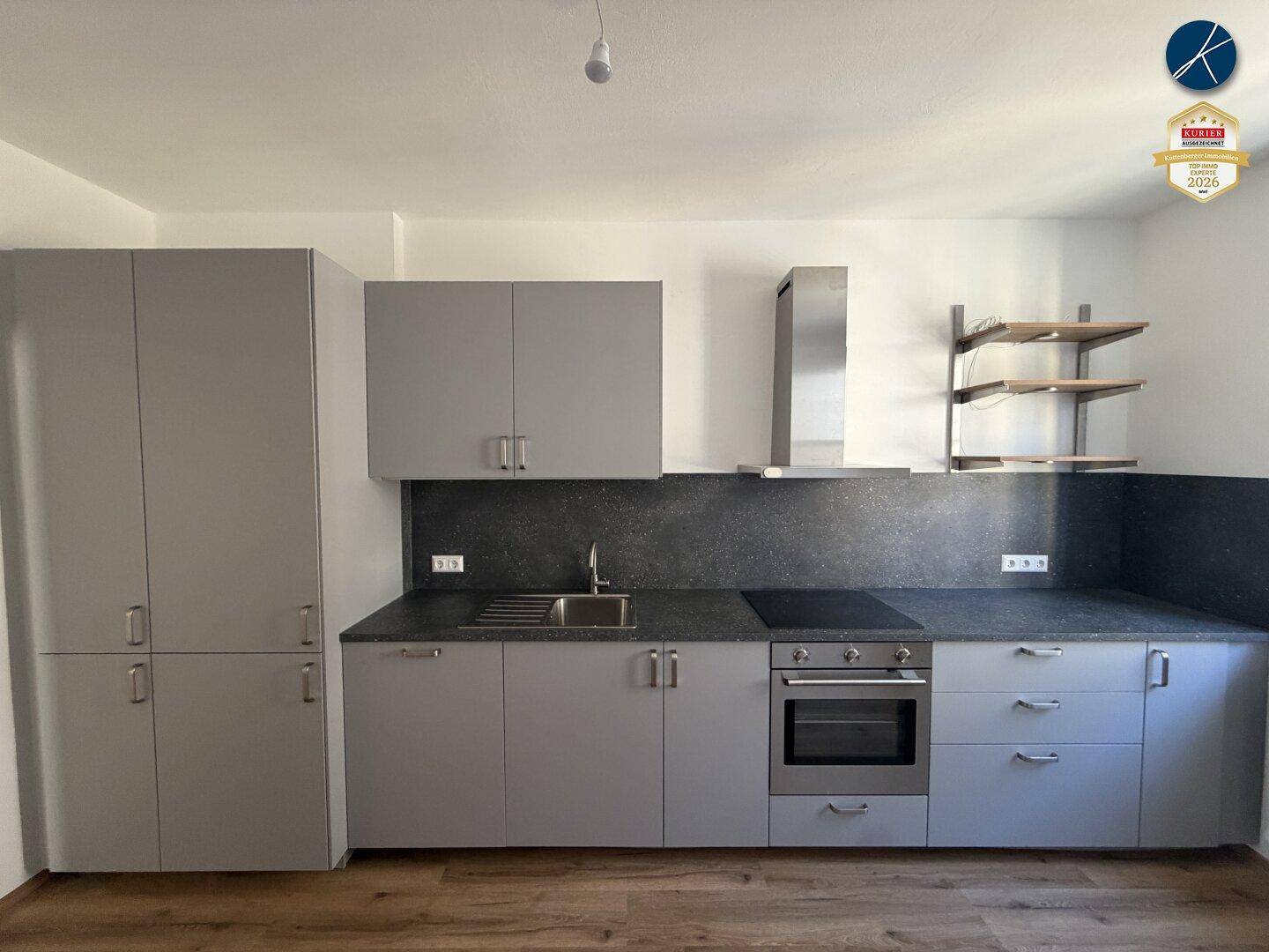 Moderne Einbauküche in Grau mit Kochfeld, Backofen und Dunstabzugshaube, unbenutzt.