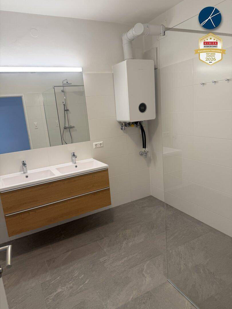 Modernes Badezimmer mit Doppelwaschbecken, großer ebenerdiger Dusche und hellen Fliesen.
