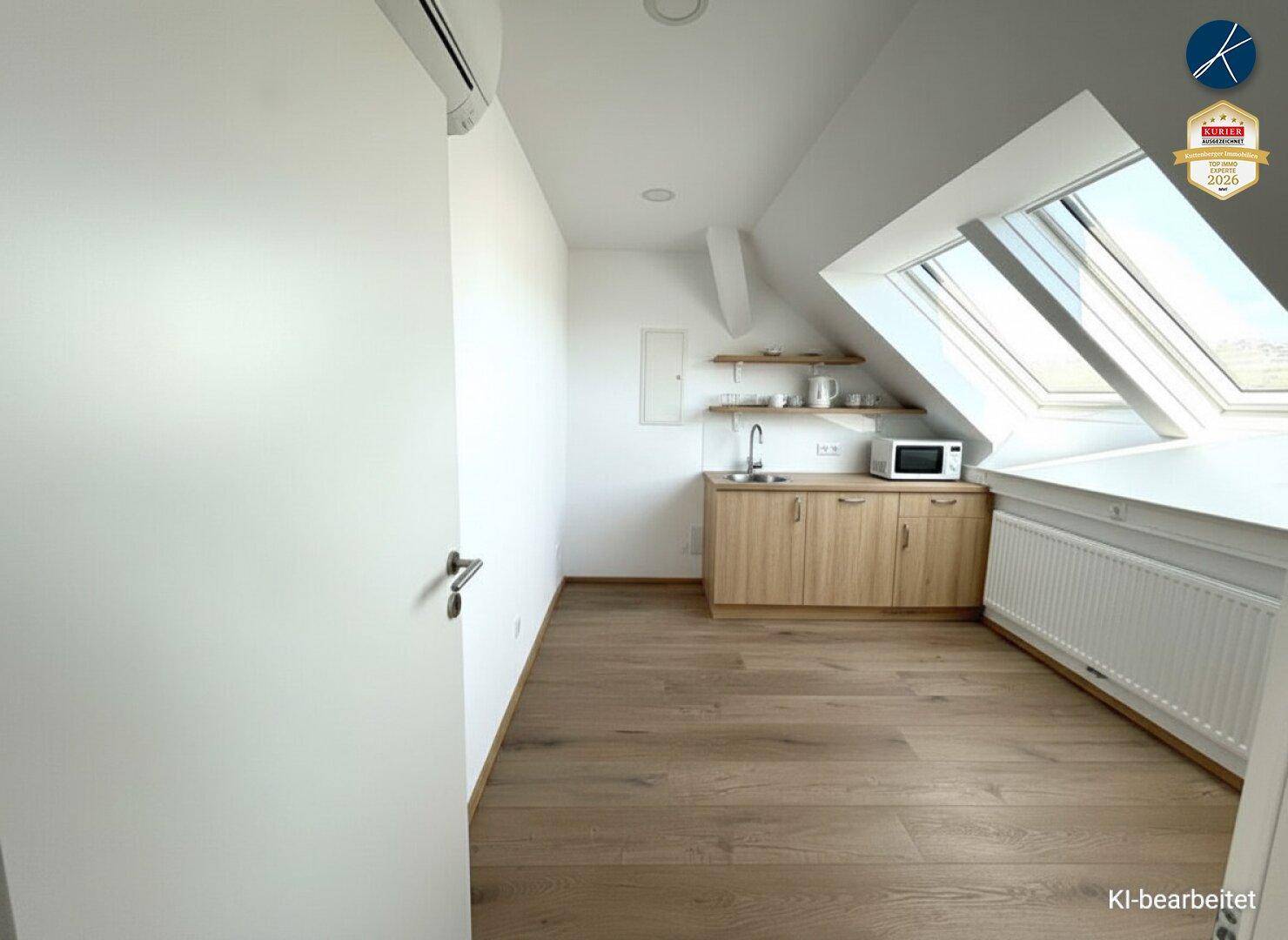 Kleine Teeküche in einem Dachzimmer mit Holzschränken, Mikrowelle und Dachfenster.