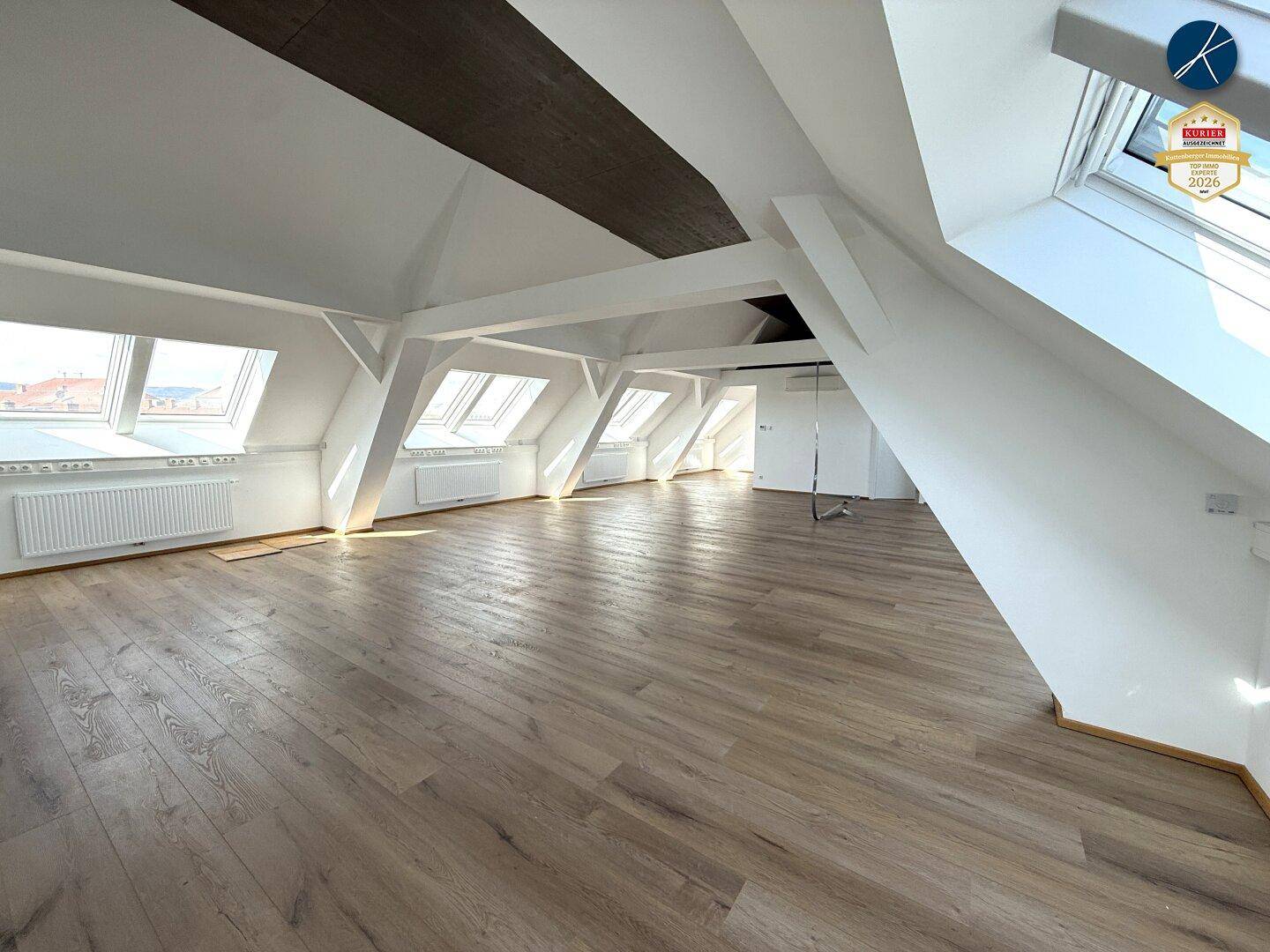 Heller Dachbodenraum mit schrägen Wänden, sichtbaren Balken und natürlichem Lichteinfall durch Dachfenster.