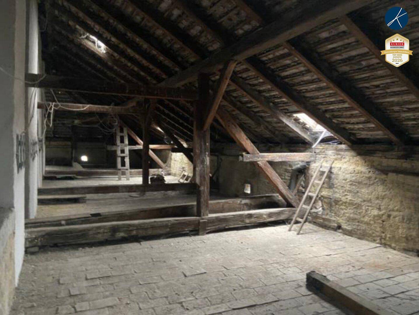 Geräumiger Dachboden mit sichtbaren Holzbalken, schrägen Dächern und einem Dachfenster.