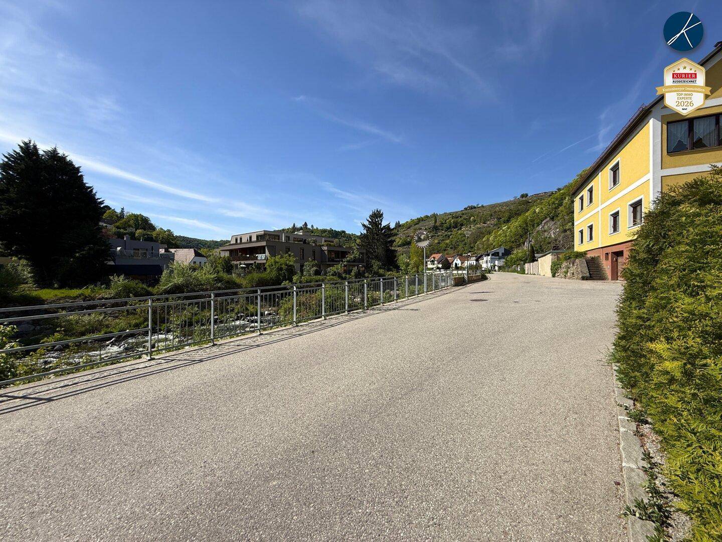 Ruhige Straße mit Häusern und grünen Hügeln, die eine ländliche Umgebung zeigen.