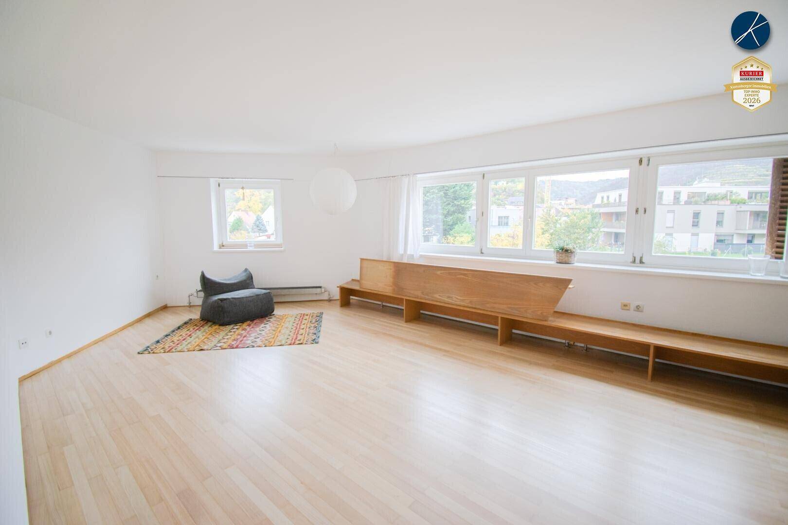 Helles Wohnzimmer mit Holzboden, großen Fenstern und Blick ins Grüne.