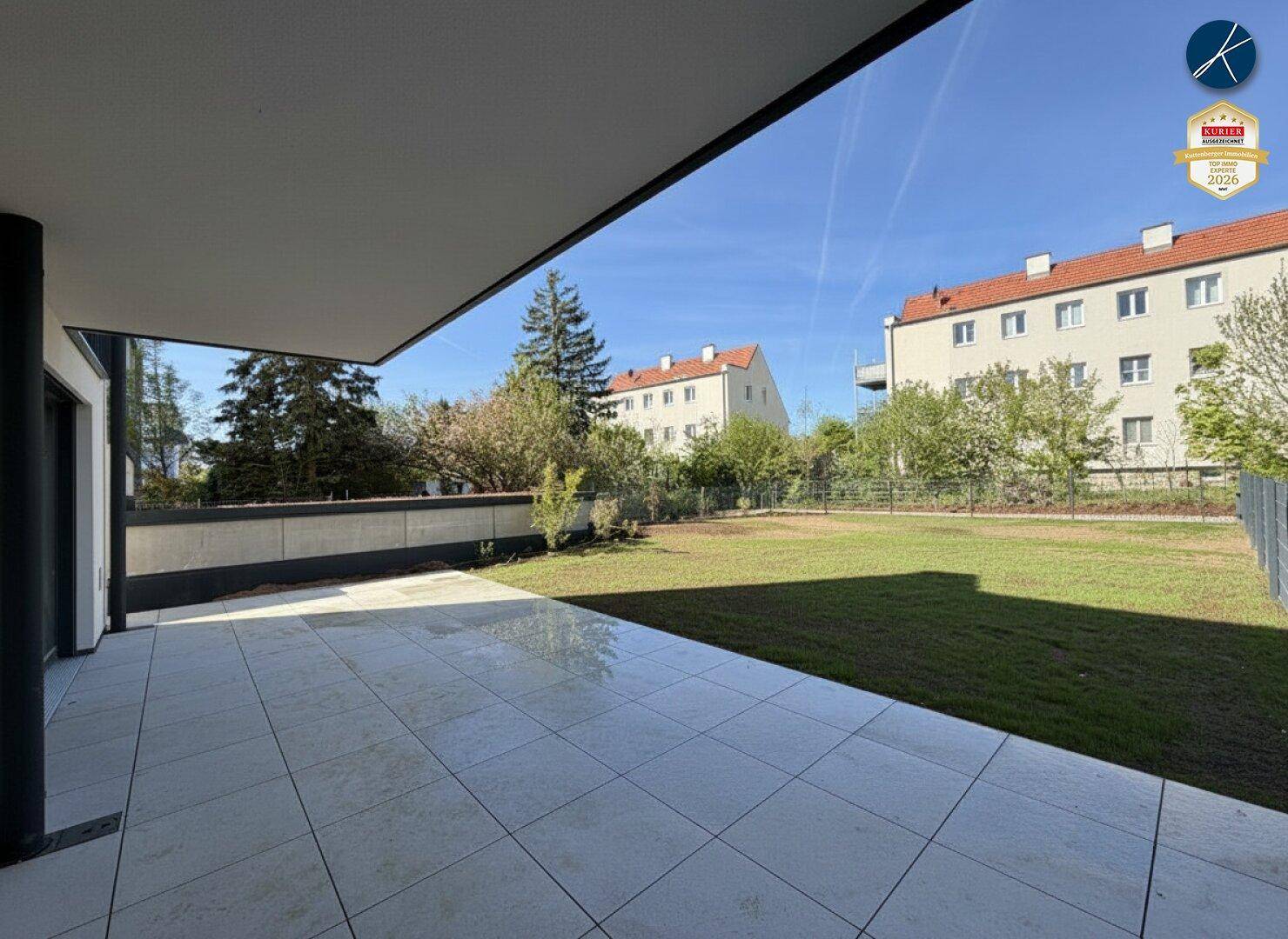 Weitläufige Terrasse mit Blick auf den grünen Garten und die benachbarten Gebäude.