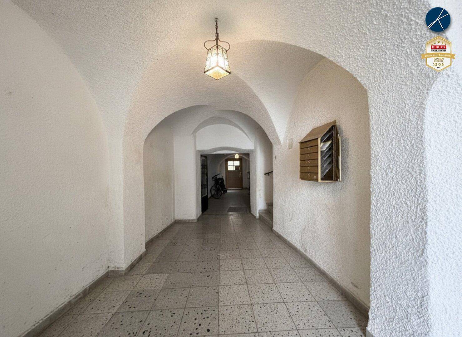 Langer Flur mit gewölbter Decke und gemustertem Fliesenboden, beleuchtet von einer Hängelampe.
