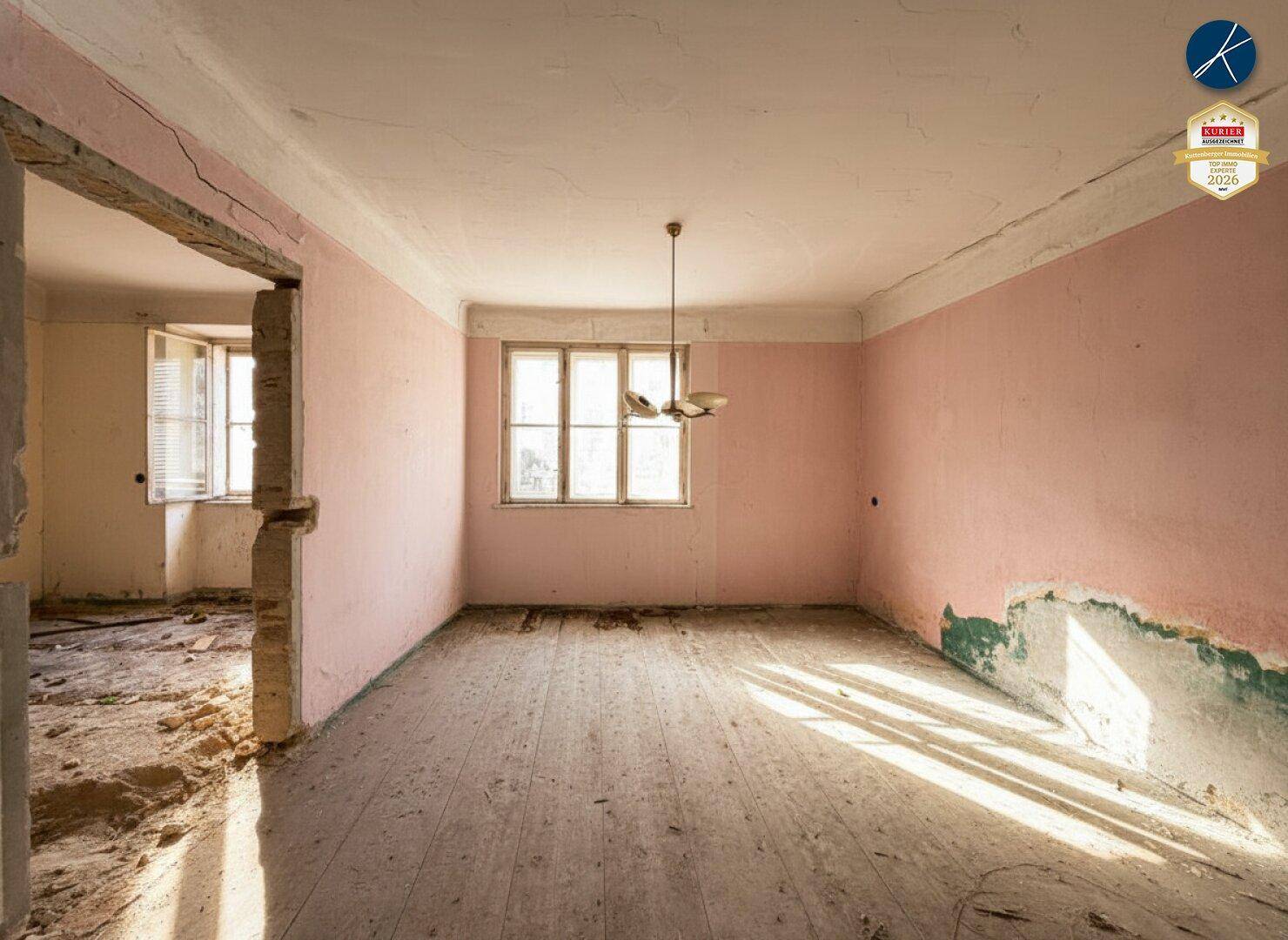 Renovierungsbedürftiger Raum mit rosa Wänden und Holzdielenboden, mit einem Durchgang zu einem weiteren Bereich.
