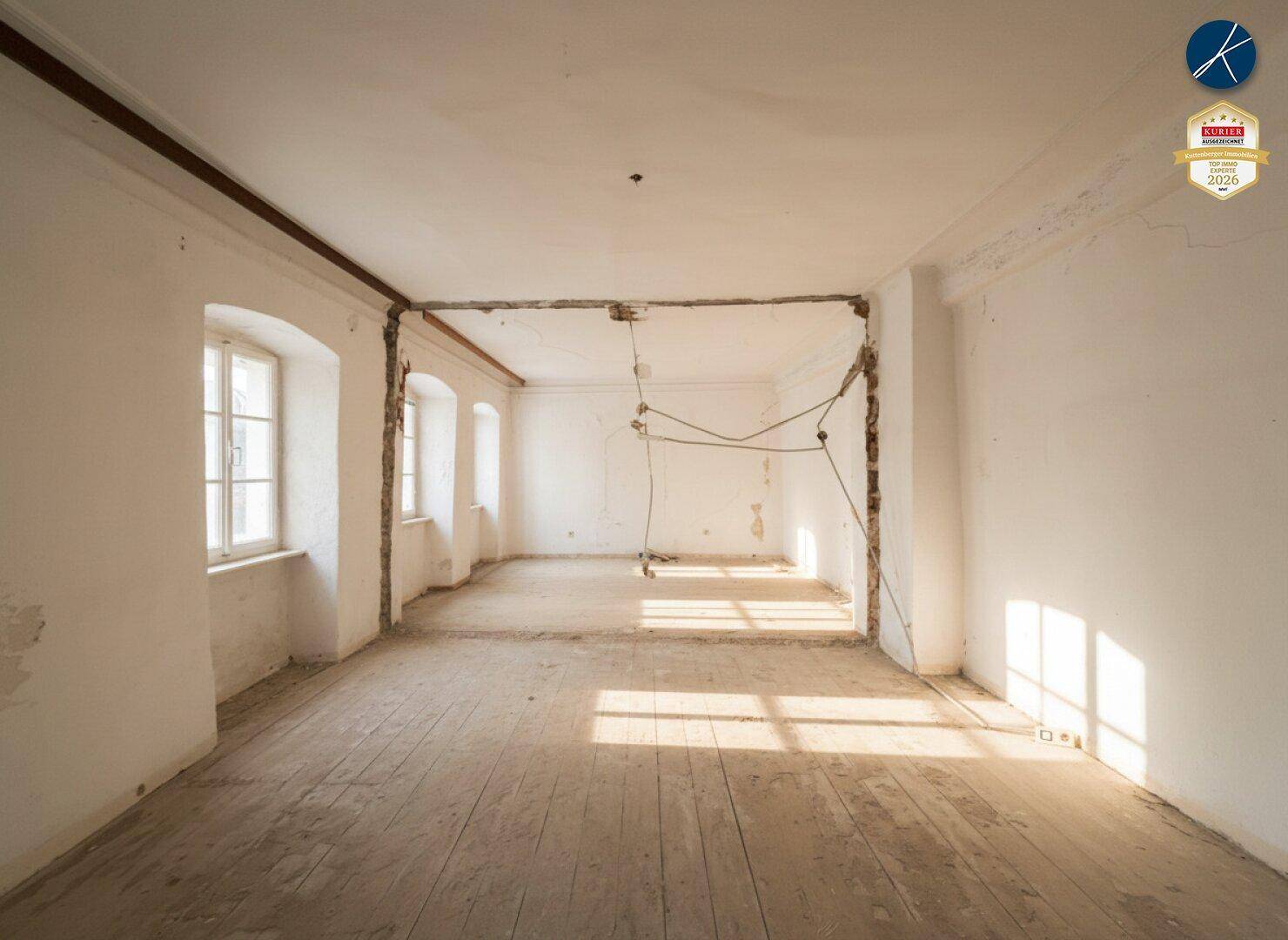 Leerer Raum in Renovierung mit freigelegten Wänden und Holzdielenboden, durchflutet von Sonnenlicht.