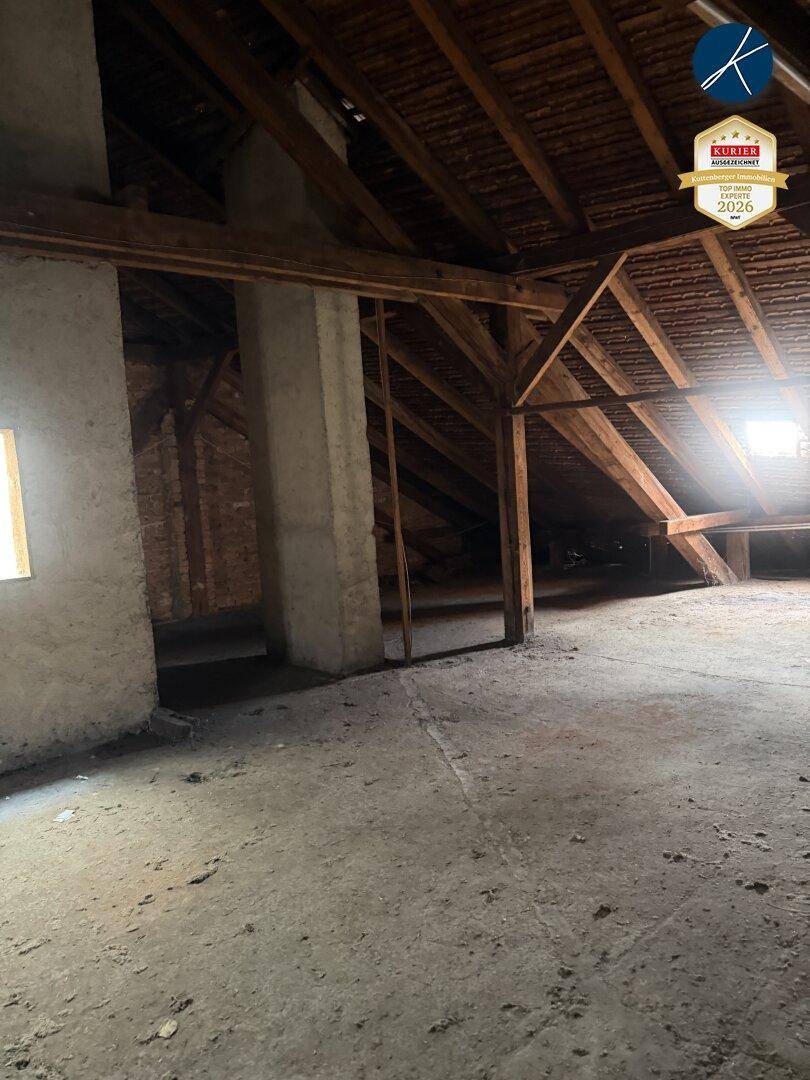 Unausgebauter Dachboden mit sichtbaren Holzbalken und Betonboden, bietet Potenzial für Ausbau.