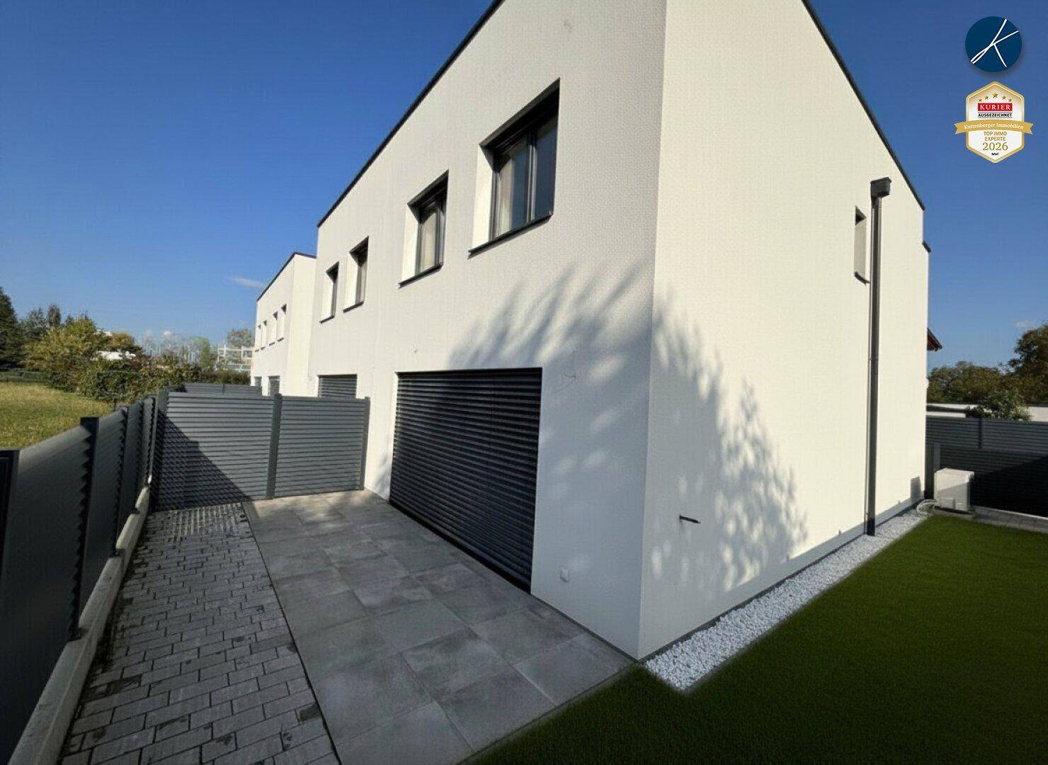 Moderne Hausfassade mit weißem Putz und gepflastertem Bereich neben dem Gebäude.